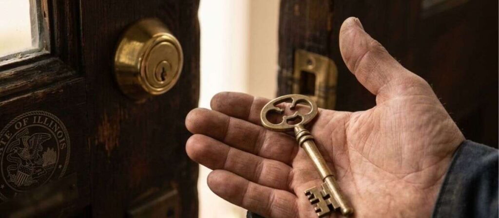A hand holds an ornate brass key near a wooden door lock. Illinois State Seal visible. Serving Urbana, IL for your locksmith needs.